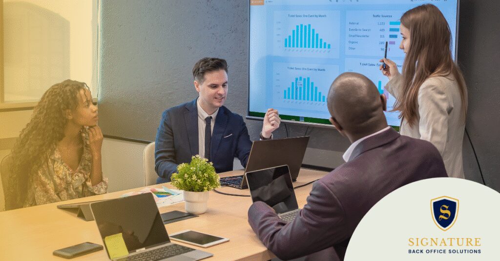A team of professionals in a meeting room reviews a presentation on navigating multi-state employment laws, with laptops and charts on display.
