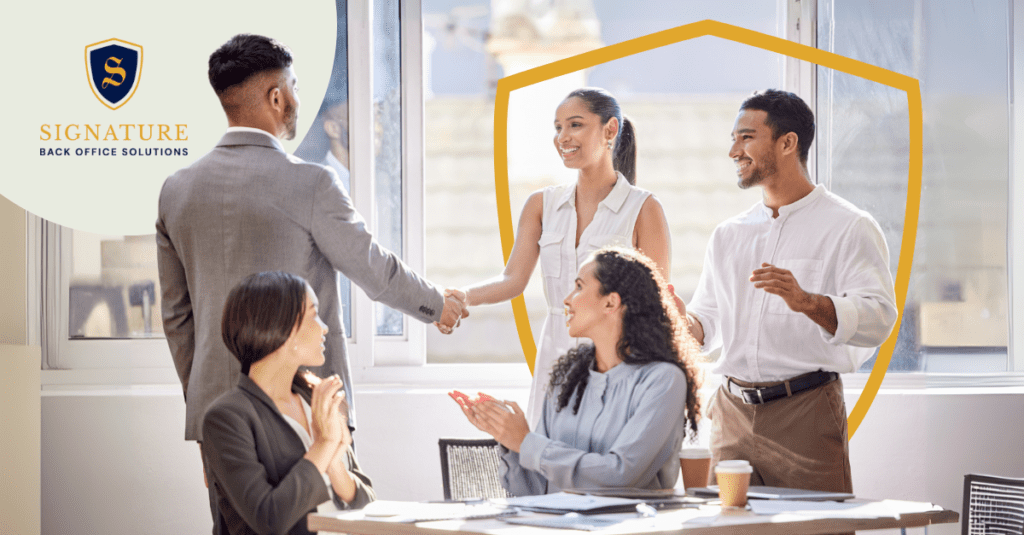 Four professionals in an office, two shaking hands while others smile and applaud; highlighting expertise in contract staffing solutions.